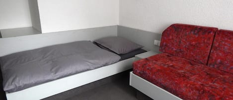 A room with a bed, a red sofa, and a wall-mounted light fixture.