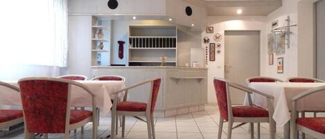 A dining area with a bar, red upholstered chairs, and a tiled floor.