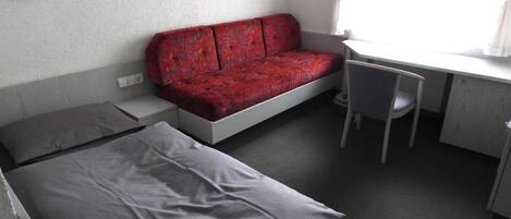 A small, compact room with a bed, a red sofa, a desk, and a chair.