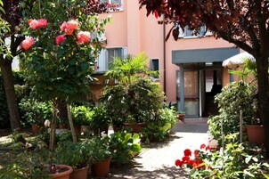Un jardín con plantas en macetas y flores que conduce a la entrada de un edificio.
