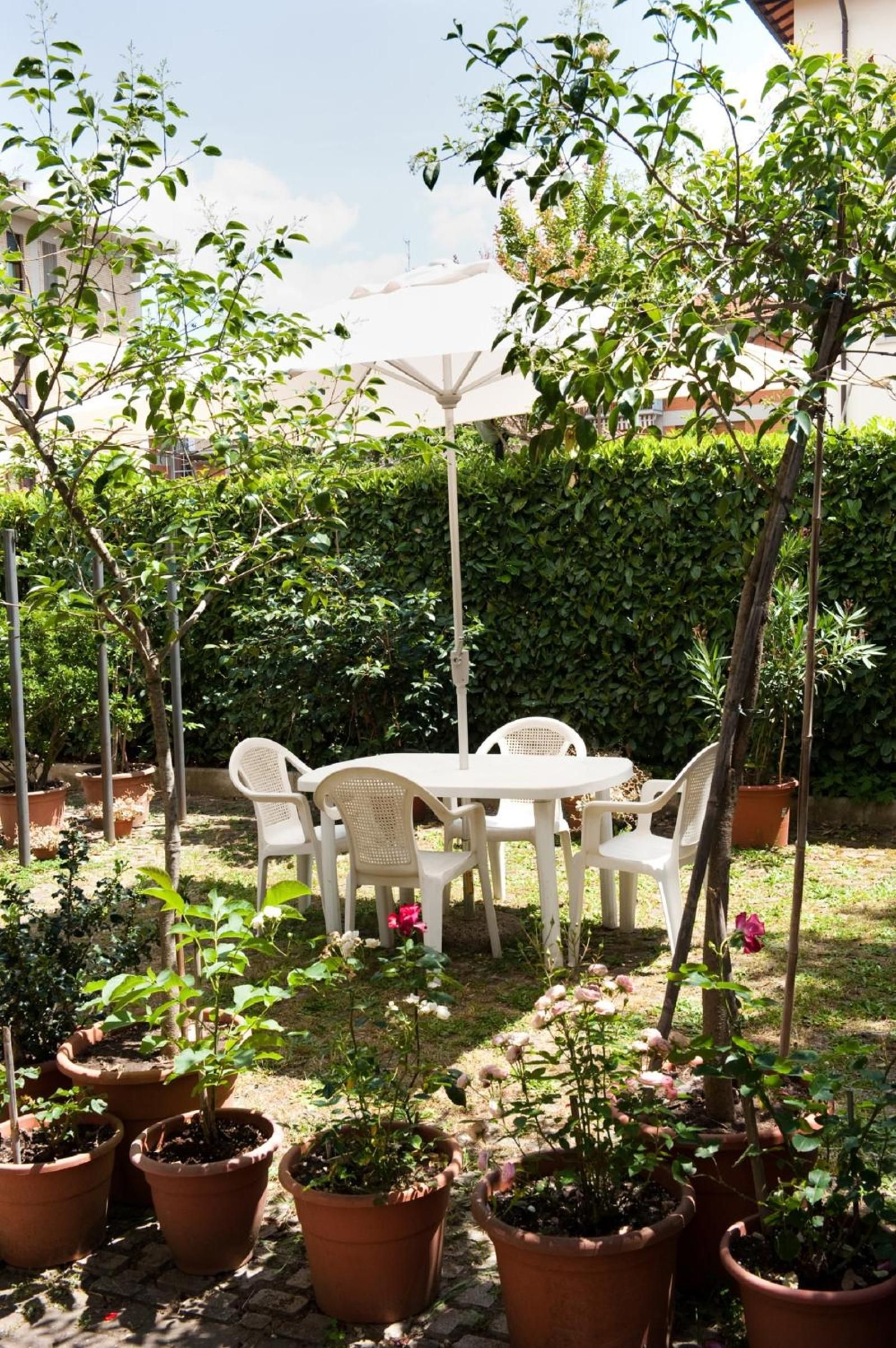 An outdoor patio with a round table and chairs, surrounded by potted plants and a white umbrella.