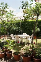 Un patio al aire libre con una mesa redonda y sillas, rodeado de plantas en macetas y un paraguas blanco.