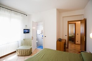 Quarto de hotel com cama, área de estar, televisão e banheiro visível por uma porta aberta.