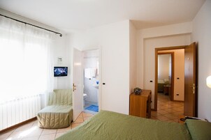 Habitación de hotel con cama, zona de estar, televisor y baño visible a través de una puerta abierta.