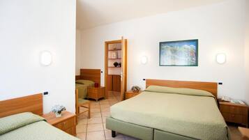 Una camera d'albergo con un letto grande, un letto più piccolo, una scrivania, una sedia, un comodino, un armadio e un quadro appeso al muro.