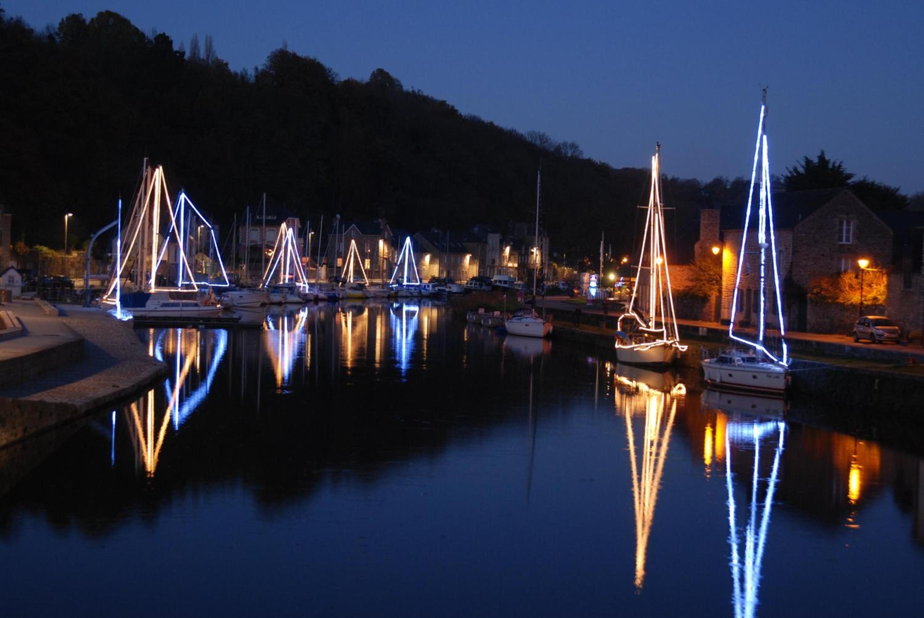 Un port de plaisance au crépuscule, avec des voiliers amarrés et leurs reflets sur l’eau.