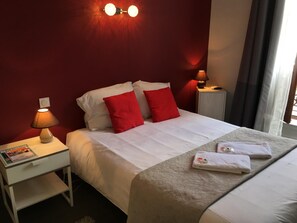 Una habitación de hotel con una cama, dos lámparas de noche, una mesita de noche con una revista y una ventana con cortinas.