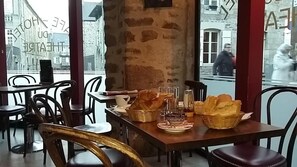 Un comedor con mesas y sillas, un pilar de piedra y vista a la calle.
