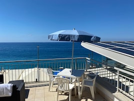 Una terraza con mesa y sillas, con vistas a una piscina y al mar.