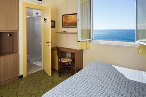 Una habitación con cama, escritorio, silla, ventana con vista al mar y puerta que da a una ducha.