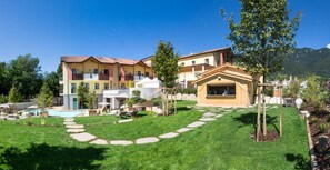 Un hotel de varios pisos con piscina, mobiliario exterior y un camino de piedra.