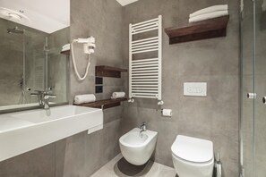 Un baño moderno con un lavamanos grande de color blanco, un bidé, un inodoro y una cabina de ducha con paredes de vidrio.