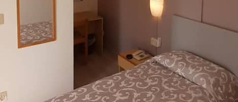 A bedroom with a bed, a ceiling fan, a wall-mounted light, and a mirror.