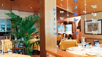 Interno di un ristorante con tavoli apparecchiati, una grande pianta in vaso e decorazioni a forma di farfalla sul soffitto.