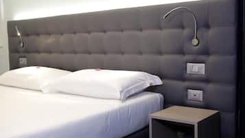 Un letto rifatto con lenzuola bianche e due cuscini, un comodino con una lampada e un punto luce a parete.