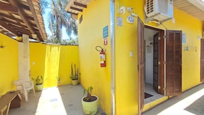 A yellow building with a wooden door, a fire extinguisher, and potted plants. - Suítes Cantinho Do Sossego Em Ubatuba (Ubatuba)