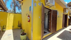 A yellow building with a fire extinguisher mounted on the wall, a door leading inside, and potted plants outside. - Suítes Cantinho Do Sossego Em Ubatuba (Ubatuba)