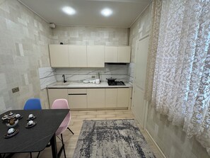 A compact kitchen with a sink, stove, and cabinets. There is a dining table with chairs and a decorative rug. - Modern 2-Bedroom Apartment · Fully Equipped (Тоshkent)
