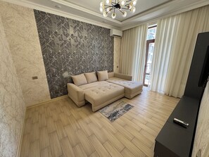 A modern living room with a sectional sofa, a flat-screen TV, and a patterned wall. - Modern 2-Bedroom Apartment · Fully Equipped (Тоshkent)
