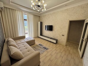 A modern living room with a sectional sofa, a flat-screen TV mounted on the wall, and a wooden floor. - Modern 2-Bedroom Apartment · Fully Equipped (Тоshkent)