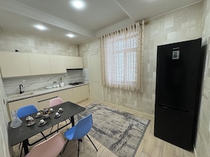 A compact kitchen with a dining area, a black refrigerator, and a patterned rug. - Modern 2-Bedroom Apartment · Fully Equipped (Тоshkent)
