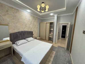 A bedroom with a bed, bedside tables, a wardrobe, a mirror, and a ceiling light fixture. - Modern 2-Bedroom Apartment · Fully Equipped (Тоshkent)