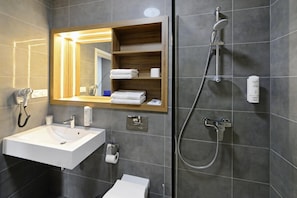 A modern bathroom with a white sink, a mirror with a wooden frame, a shower with a handheld showerhead, and a toilet.