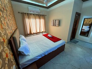 Une chambre à coucher comprenant un lit, des rideaux, un ventilateur de plafond, un appareil de climatisation et une œuvre d’art accrochée au mur.