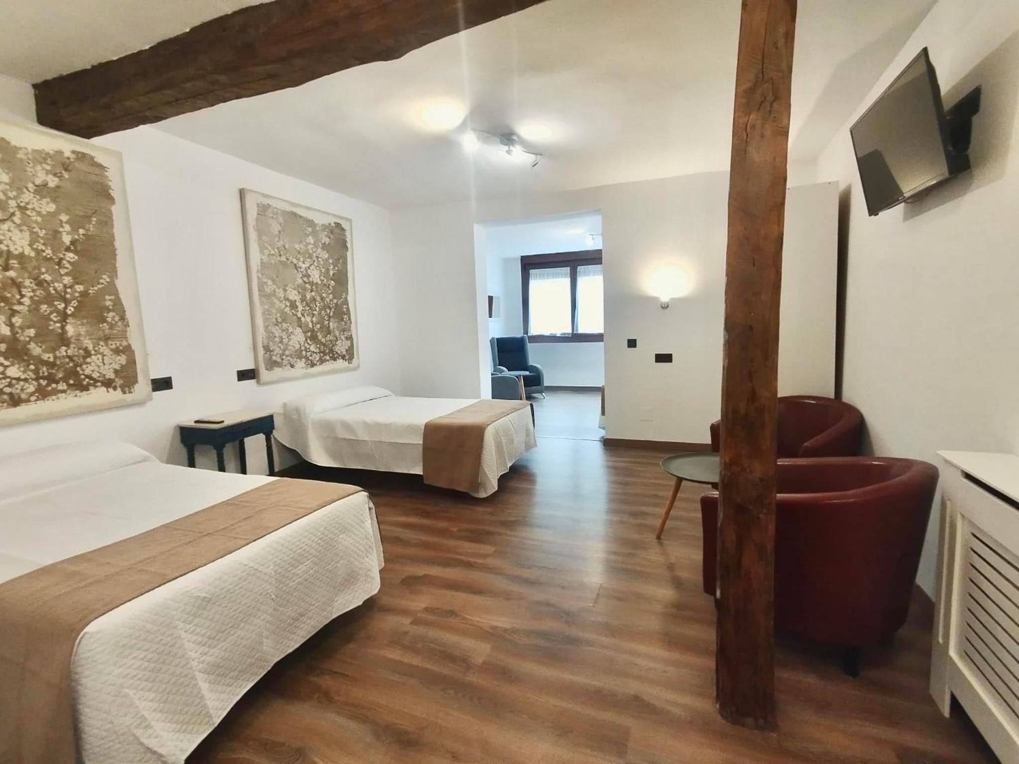 A hotel room with two beds, a TV, a wooden ceiling beam, and a view of the hallway.