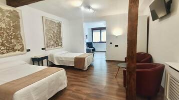 A hotel room with two beds, a TV, a wooden ceiling beam, and a view of the hallway.