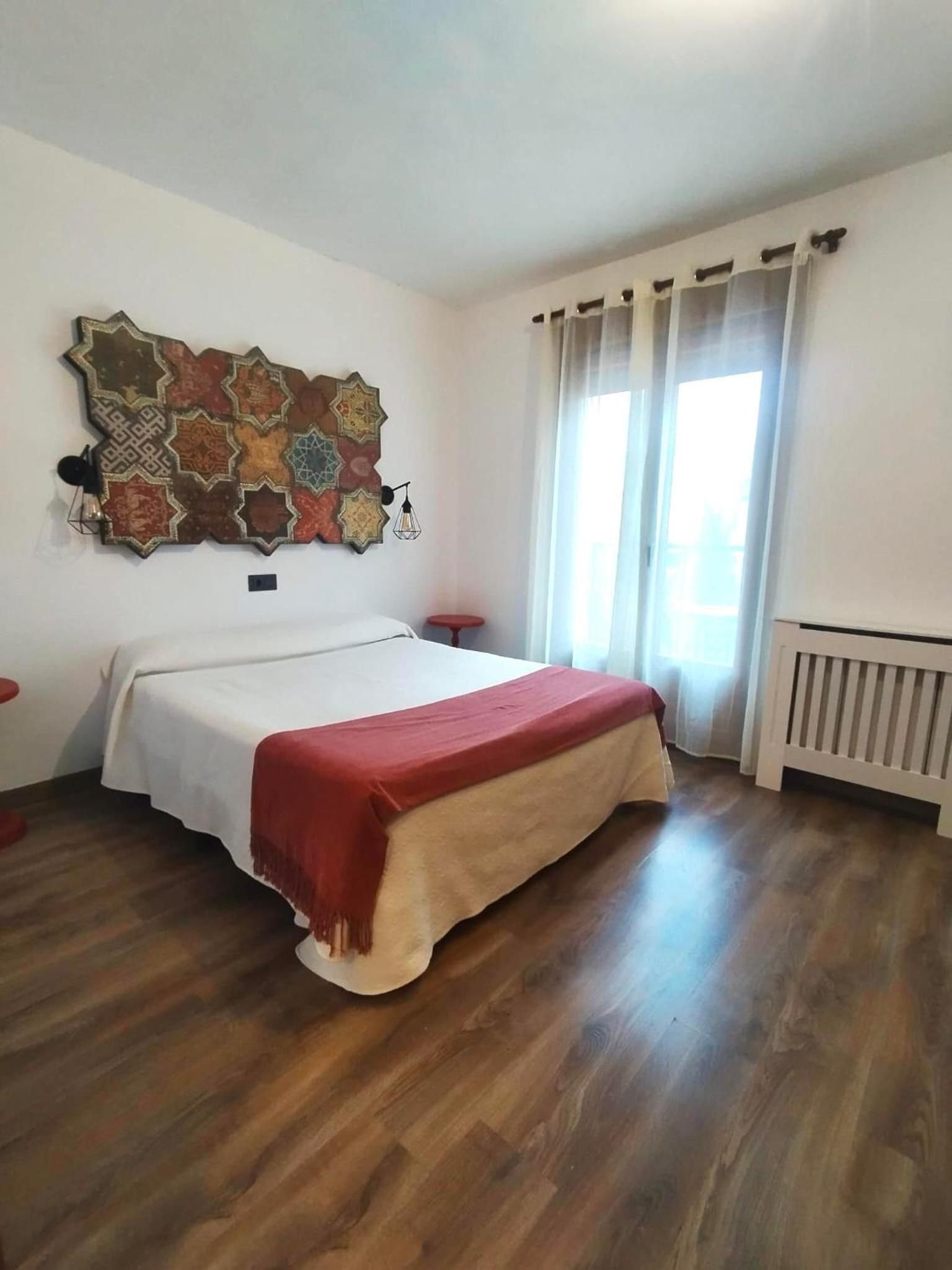 A bedroom with a bed, a wall decoration, a window with curtains, and a radiator.