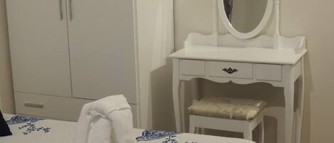 A bedroom with a bed, a white vanity with a mirror, and a wardrobe.