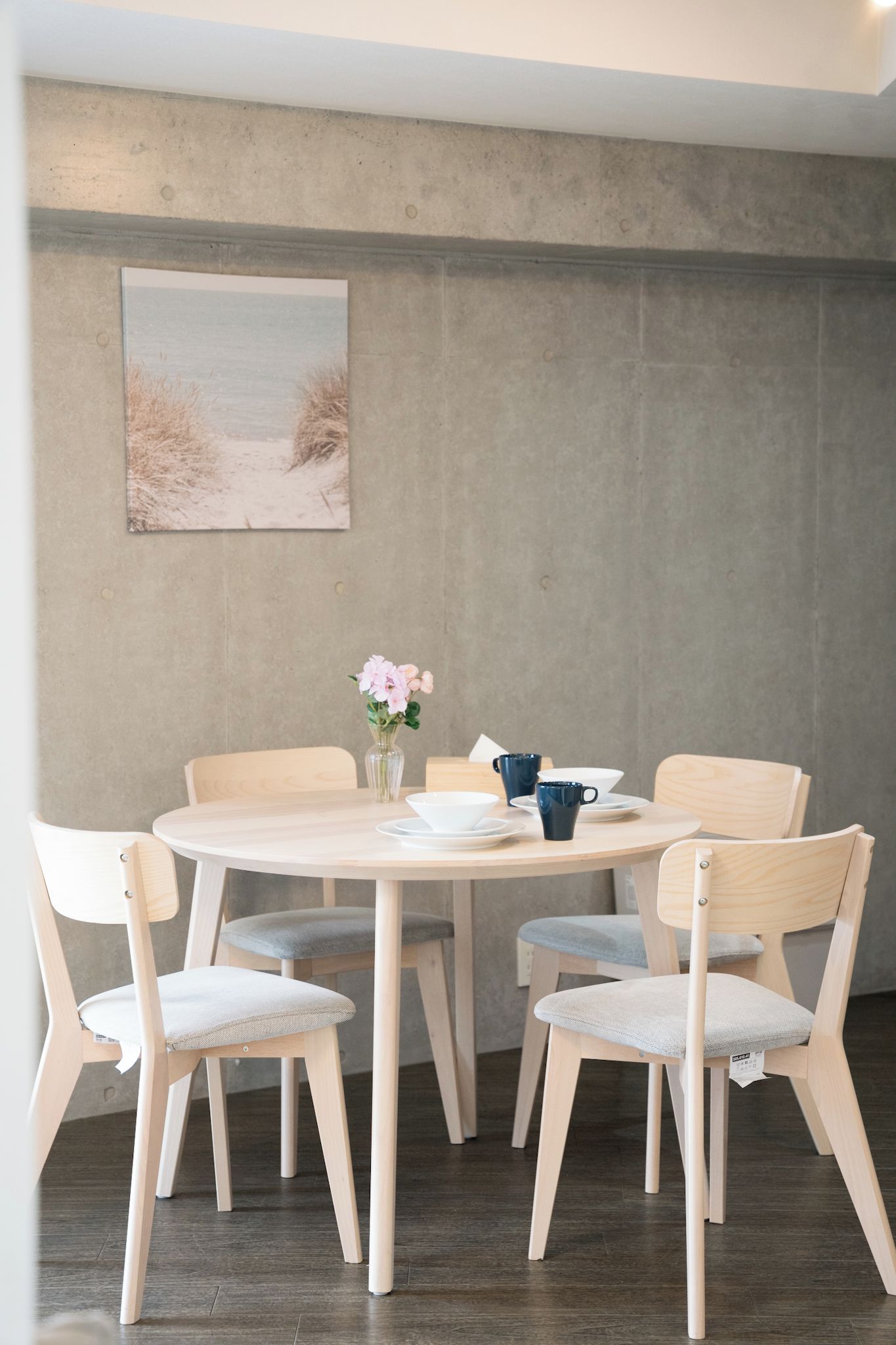 A round dining table with six chairs, a vase with flowers, and a blue mug.