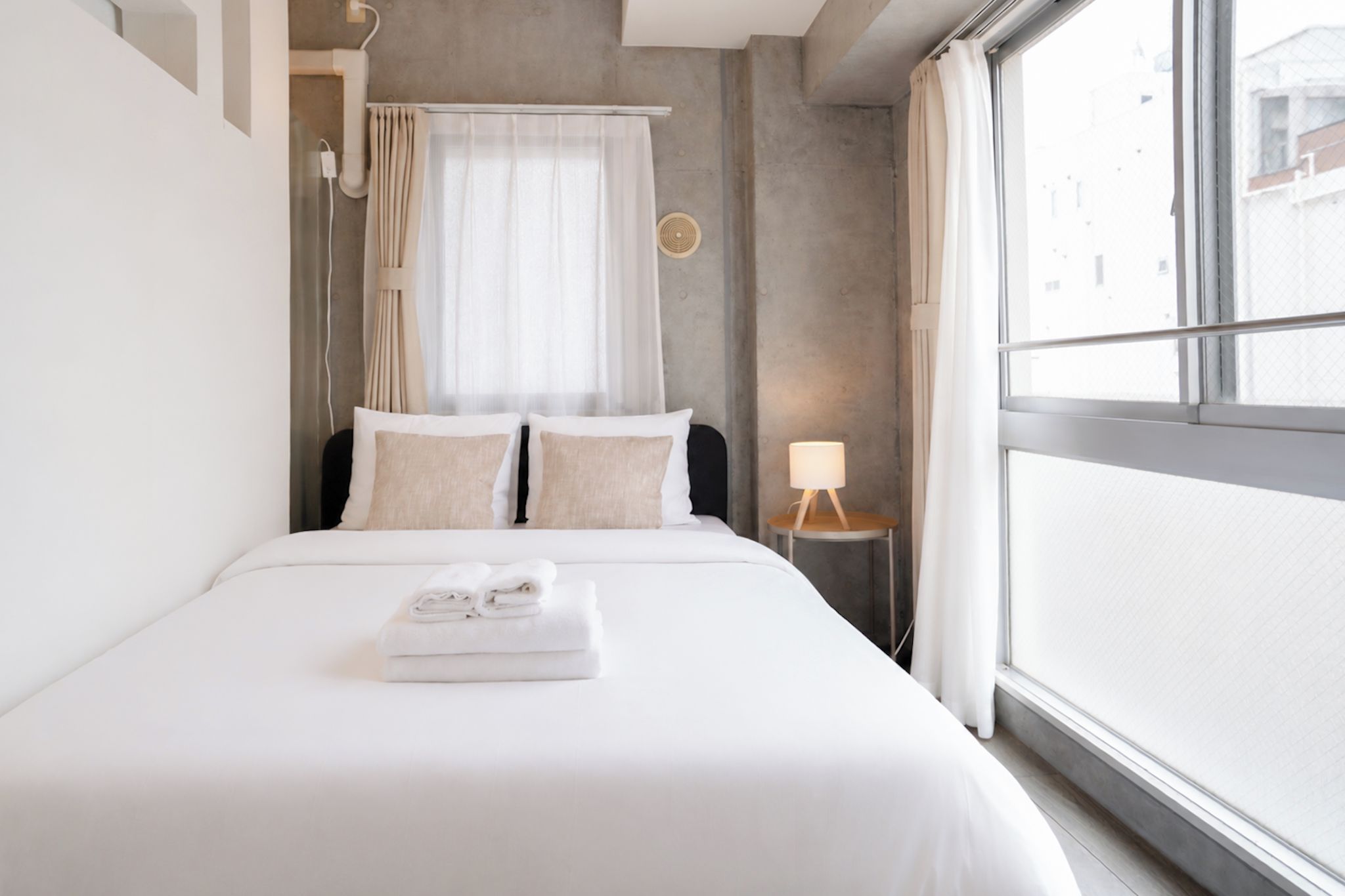 A hotel room with a bed, a nightstand, a lamp, and a view through a window.