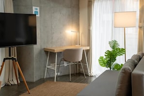 A modern room with a flat-screen TV, a desk with a chair, a lamp, a sofa, and a large plant. - HomeNest Asakusa (Taito City)