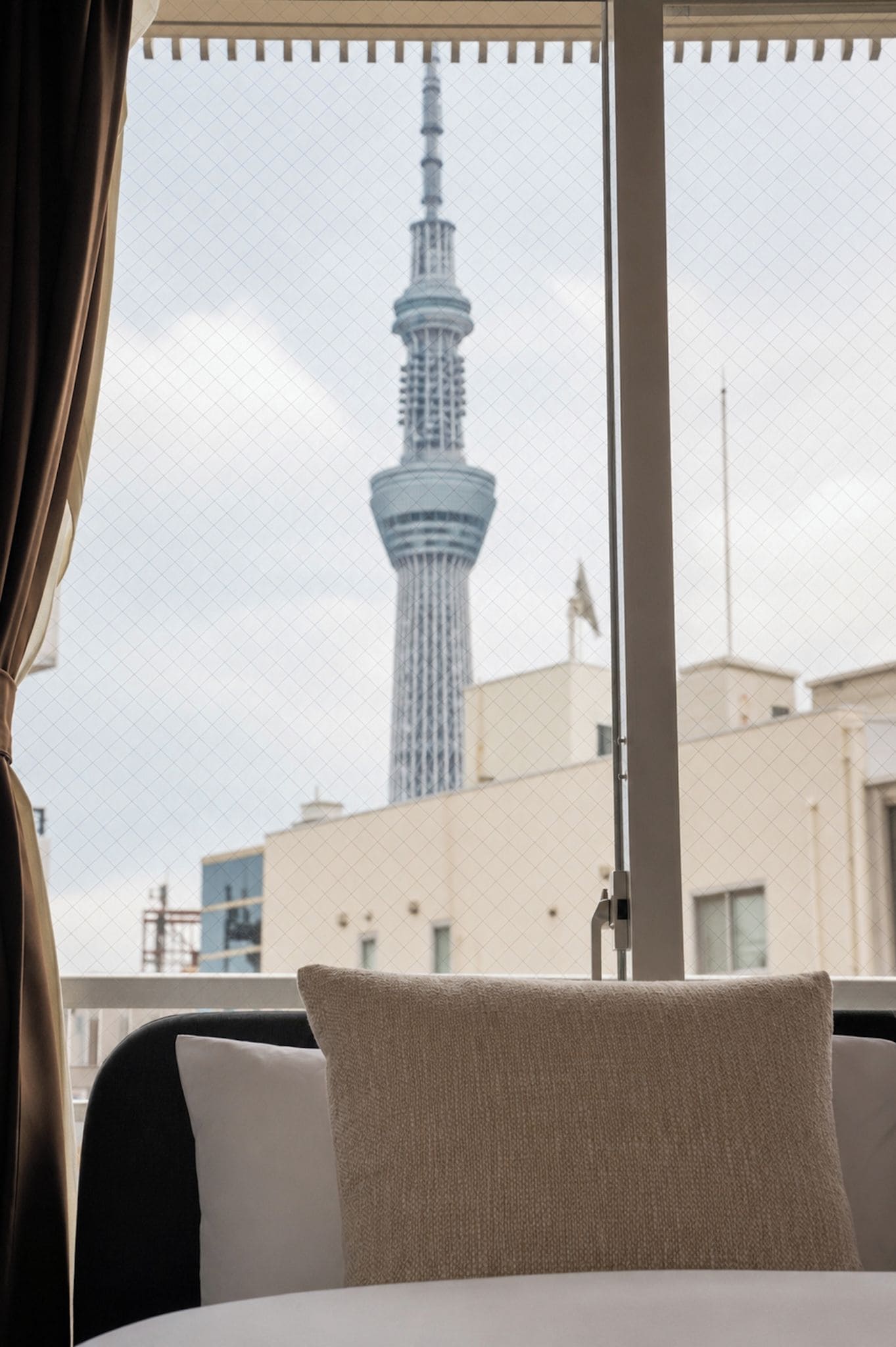 A hotel room with a bed, a window with a view of a tall tower, and a curtain.