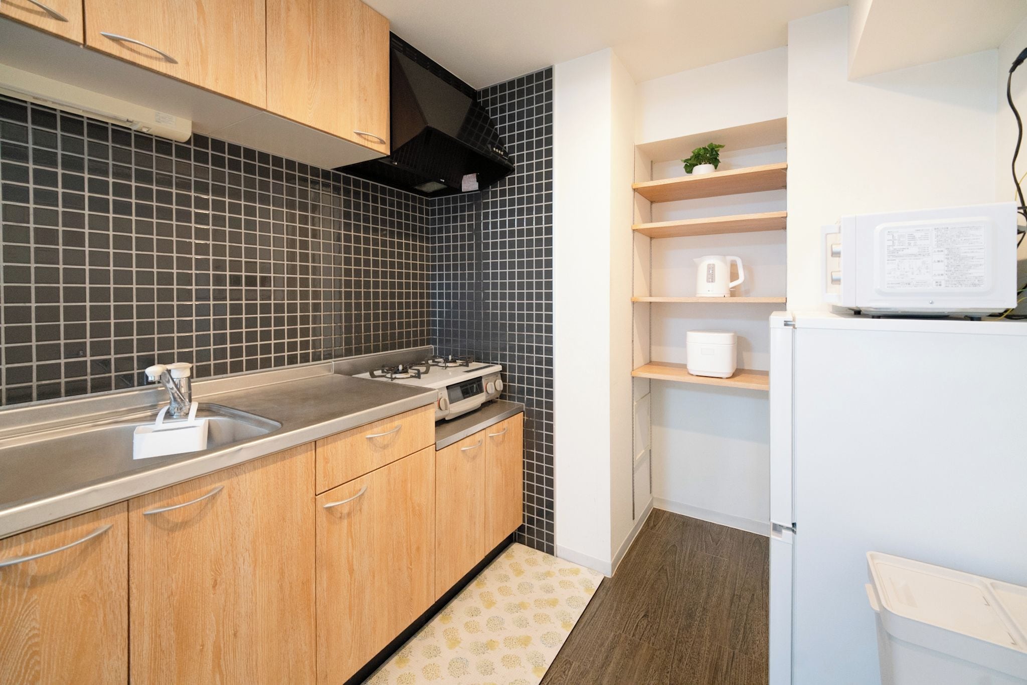 Une cuisine moderne avec des meubles en bois, une cuisinière à gaz, un four à micro-ondes et une petite étagère sur laquelle est posée une plante.