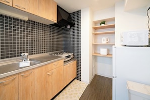 A modern kitchen with wooden cabinets, a gas stove, a microwave, and a small shelf with a plant. - HomeNest Asakusa (Taito City)