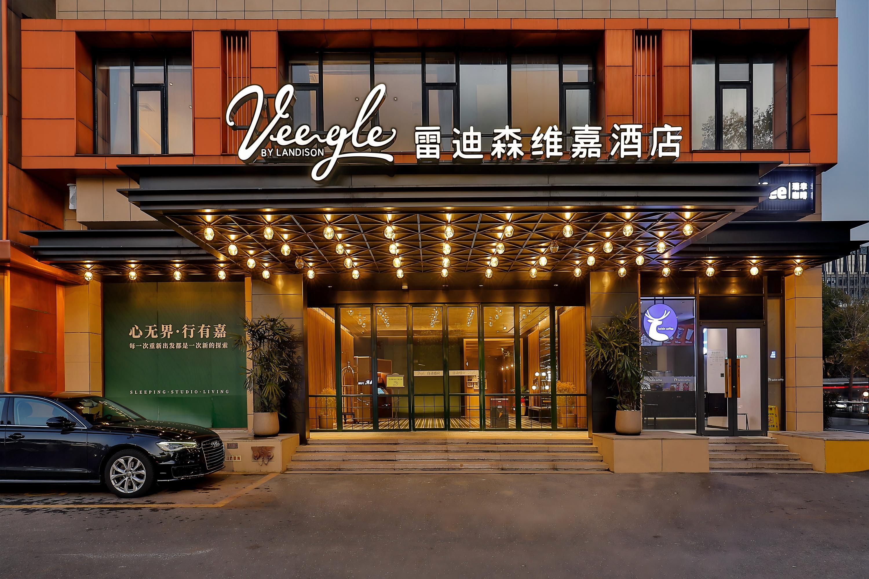 L’entrée d’un hôtel au design moderne, avec une enseigne bien visible et une voiture garée devant.