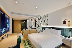 A hotel room with a bed, bedside table, a desk with a chair, a television, and a patterned wall. - Hangzhou Huanglong Sports Centre Veegle (Hangzhou)