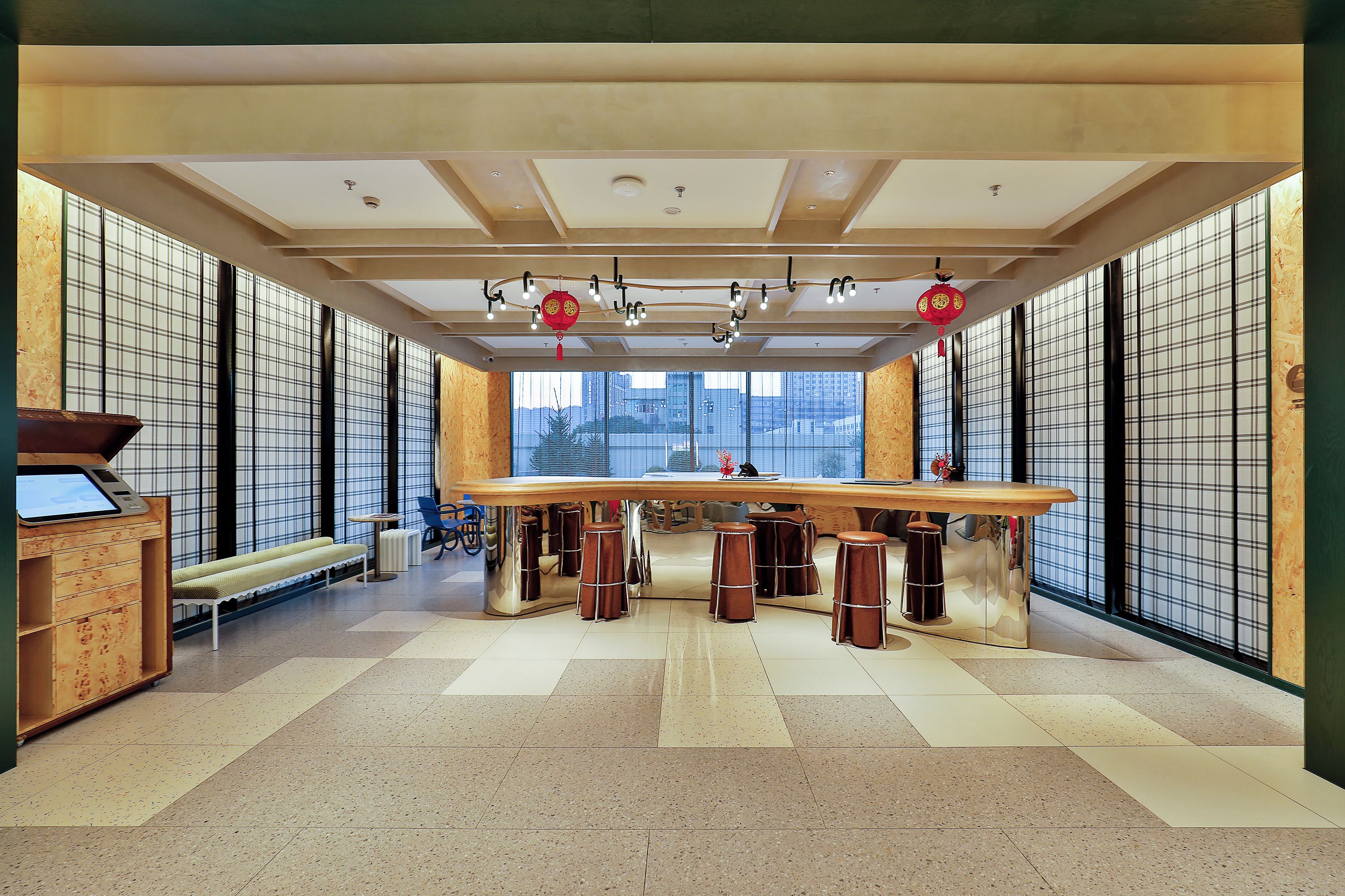 A spacious room with a long table, multiple stools, and large windows.