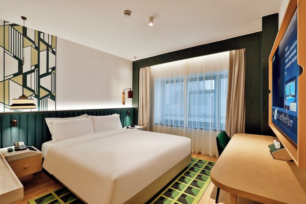 Una habitación de hotel con cama, escritorio, silla, televisor y ventana con cortinas.