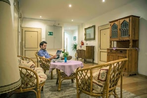 Een kamer met een eettafel, rieten stoelen, een houten kast met glazen deuren en een brandblusser.