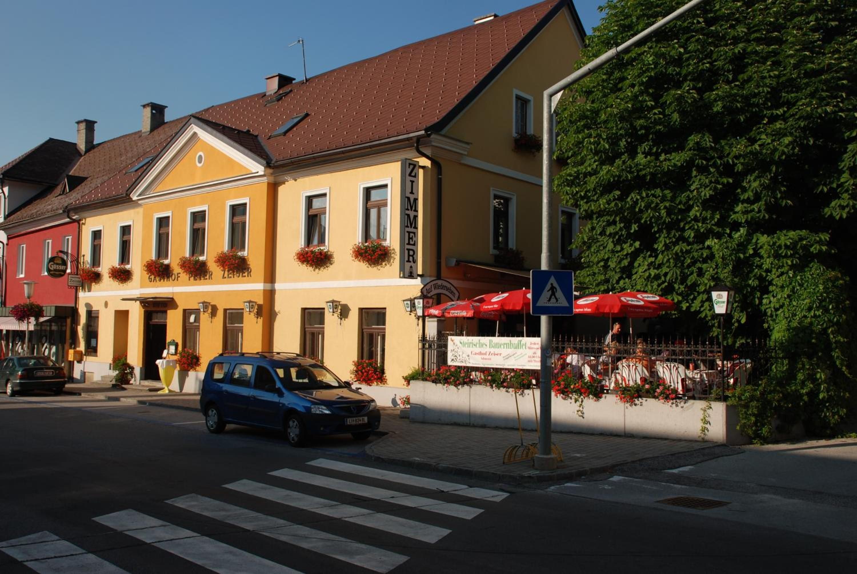 Straßenansicht mit einem gelben Gebäude, einem geparkten blauen Auto und einer Fußgängerampel.