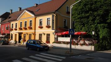 Straßenansicht mit einem gelben Gebäude, einem geparkten blauen Auto und einer Fußgängerampel.