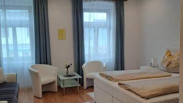 Ein modernes Schlafzimmer mit einem großen Bett, zwei Sesseln, einem kleinen Tisch und einem großen Fenster mit Vorhängen.