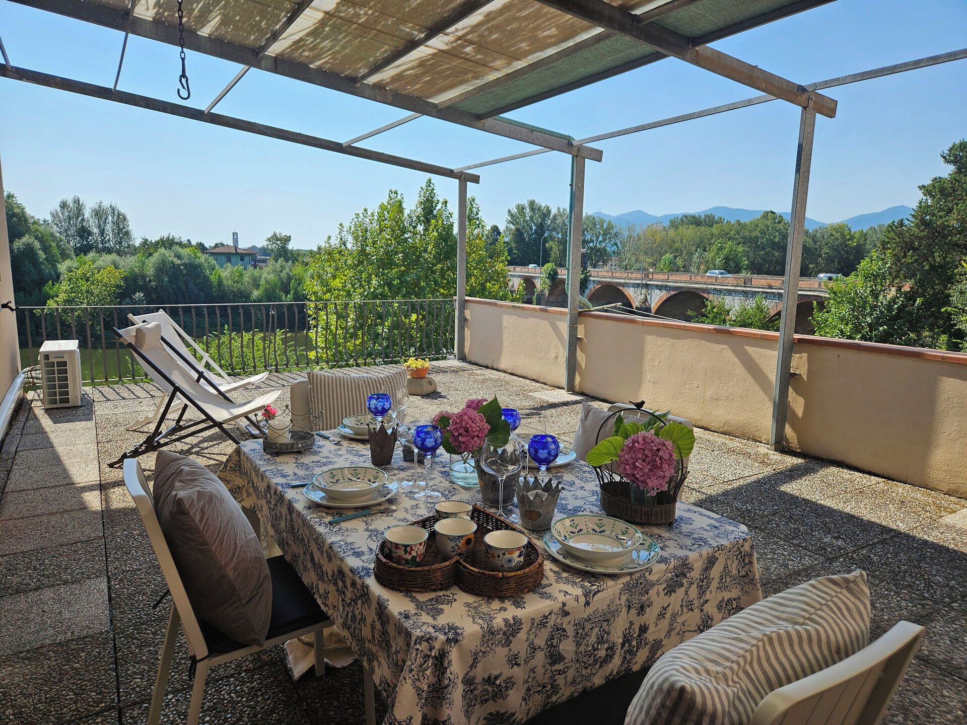 An outdoor patio with a table set for dining, surrounded by chairs, and overlooking a scenic landscape.