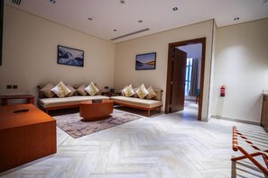 Ein modernes Hotelzimmer mit einer Sofagarnitur, einem Holztisch und einem Parkettboden mit Fischgrätmuster.