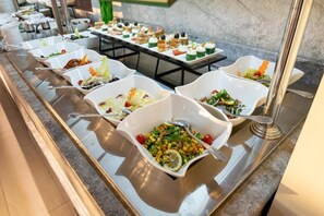 Ein Buffet mit verschiedenen Gerichten in weißen Schüsseln, angeordnet auf einer Edelstahl-Theke.
