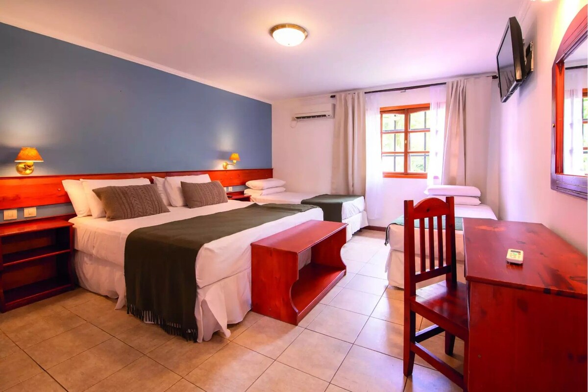 A hotel room with a bed, bedside tables, a desk, a chair, and a television.